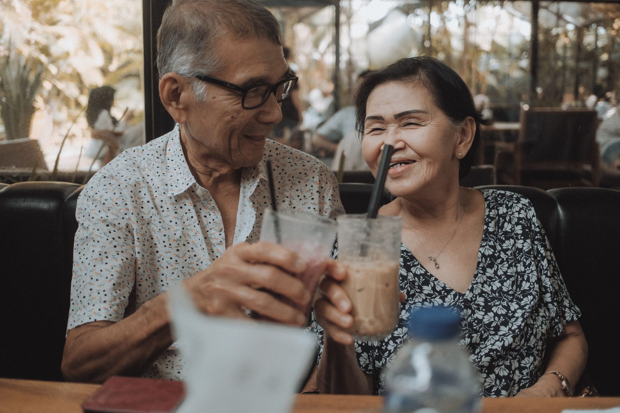 An older couple laughing over iced drinks at a cafe