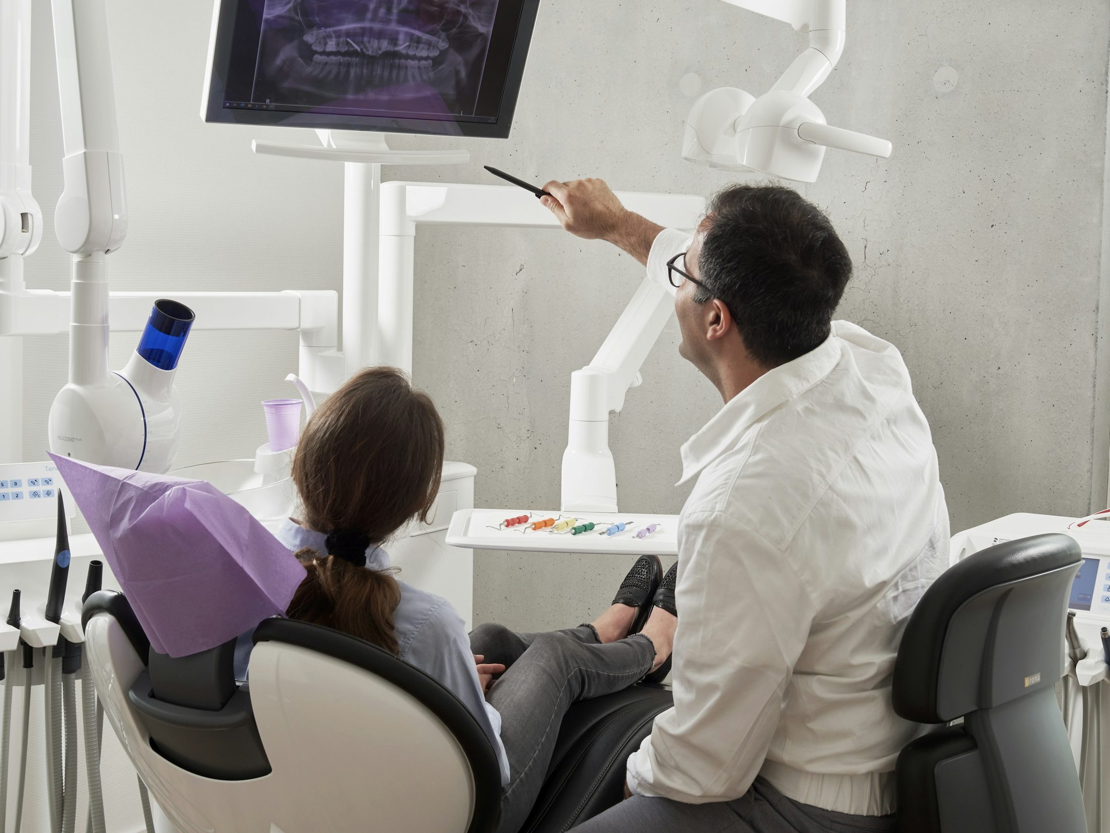 A dentist pointing out details on an X-ray to a patient in the chair